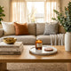 Beautifully styled rectangular oak coffee table featuring stacked hardcover books, a tall ceramic vase with greenery, and a marble tray in a sunlit modern living room.