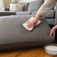 Spot cleaning a grey fabric couch cushion with a cloth and soapy water