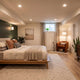 Modern basement bedroom with low-profile platform bed, layered warm lighting, and a dark green accent wall by Elax Furniture.